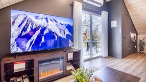 Una sala de estar moderna con un televisor de pantalla plana grande, una chimenea y un ventanal corredero que da a un espacio exterior.