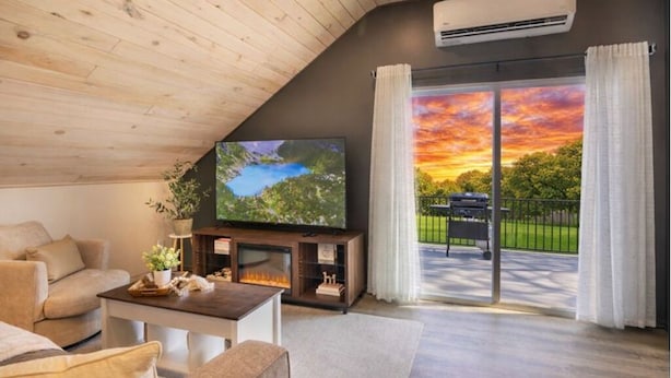 Un salón moderno con televisor de pantalla plana, chimenea y balcón con vista al atardecer.