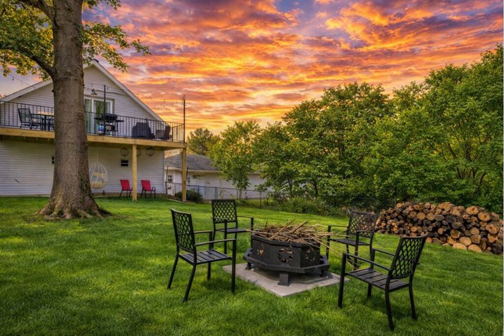 A backyard with a fire pit, chairs, and a tree.