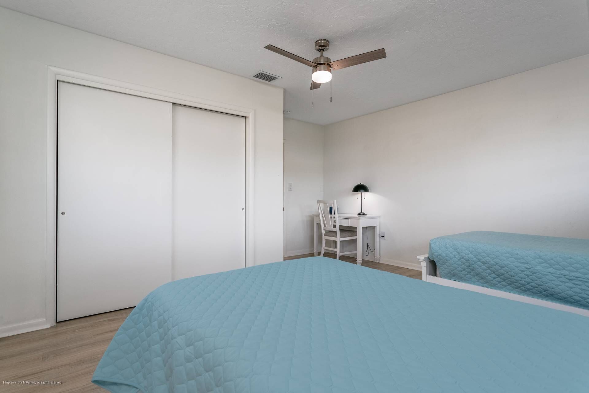 A bedroom with two beds, a desk, a chair, a ceiling fan, and a door.