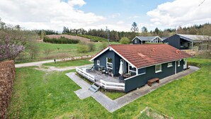 Une maison de plain-pied avec un toit recouvert de tuiles rouges, une véranda dotée de meubles d’extérieur et une petite terrasse.