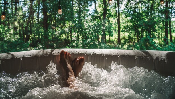 Una bañera de hidromasaje con una persona relajándose, rodeada de vistas al bosque.