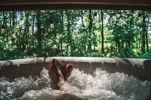 Una bañera de hidromasaje con una persona relajándose, rodeada de vistas al bosque.