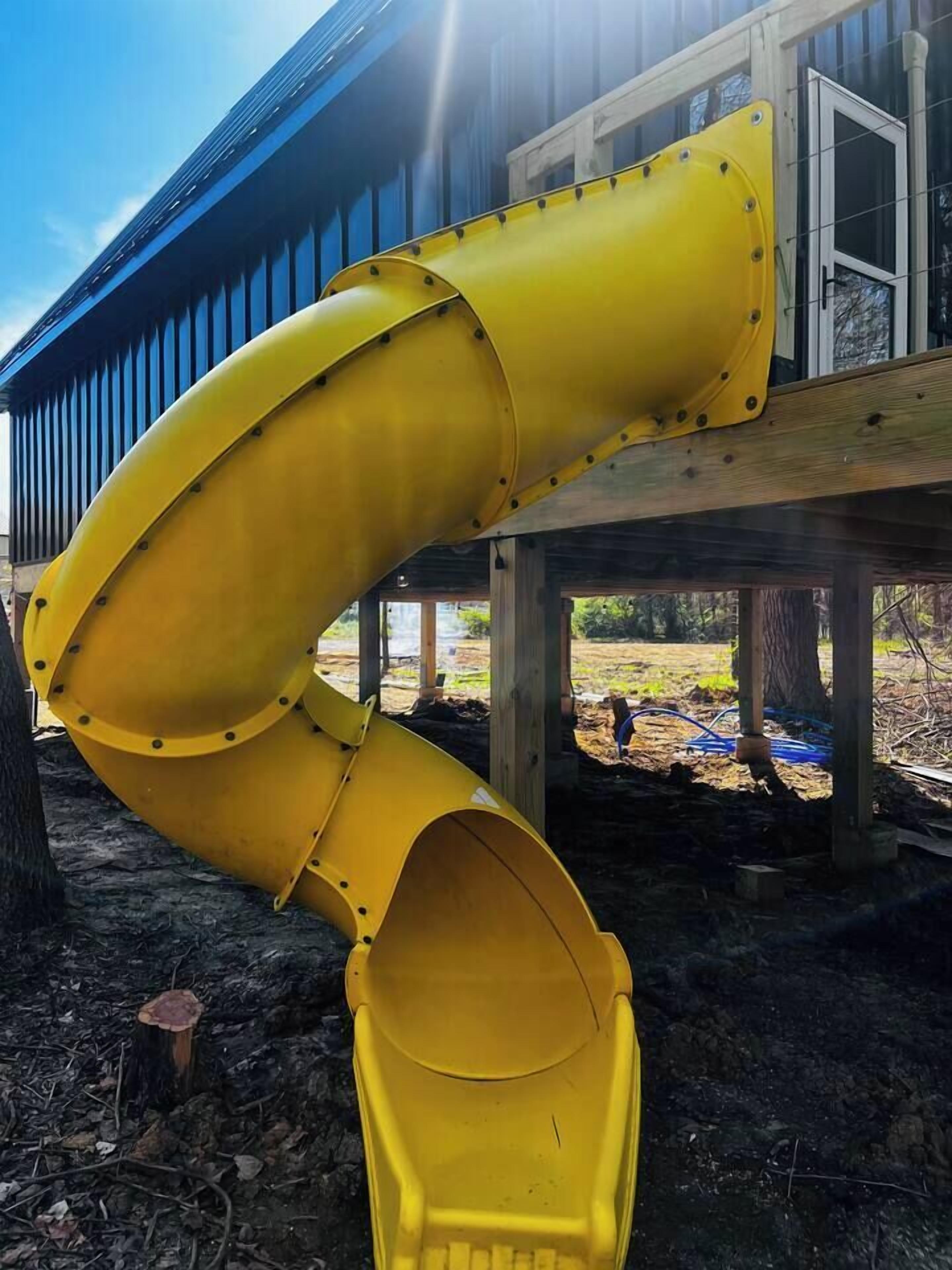 Een gele glijbaan bevestigd aan een houten terras onder een gebouw met een blauw dak.