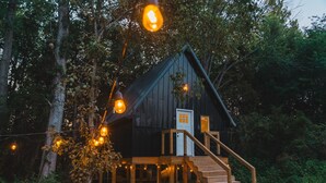 Una cabaña rústica con una terraza de madera, una escalera y luces colgantes.
