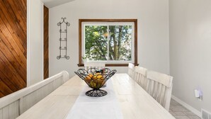 A dining area with a long table, a fruit basket, a decorative wall piece, and a window with a view of trees. - Stylish 4 level home in a quiet safe neighborhood nestled in a cul-de-sac.  (Pueblo)