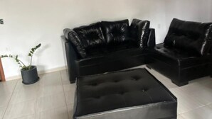 A living room with a black leather sofa and ottoman, a potted plant, and a wall-mounted artwork. - Casa Espaçosa Ubatuba (Ubatuba)