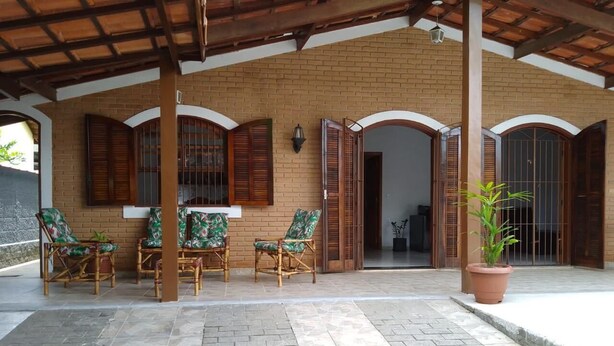 A covered patio with a brick wall, wooden shutters, and a potted plant. - Casa Espaçosa Ubatuba (Ubatuba)