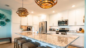 Una cocina moderna con armarios blancos, electrodomésticos de acero inoxidable, encimera de granito y taburetes de bar trenzados.