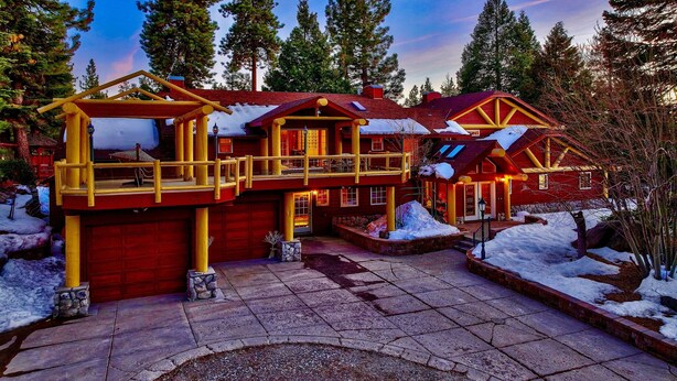 A large, multi-story log cabin with a red and yellow exterior, surrounded by snow and tall pine trees. - Luxe141 Spacious Luxury  Log Cabin (Glenbrook)