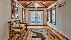 A spacious hallway with wooden beams, a chandelier, and a large rug with a bear design. - Luxe141 Spacious Luxury  Log Cabin (Glenbrook)