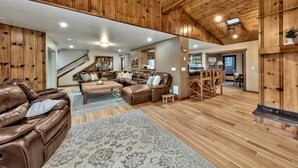 A spacious living room with a wooden ceiling, leather sofas, a coffee table, and a staircase leading to another level. - Luxe141 Spacious Luxury  Log Cabin (Glenbrook)