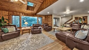 A spacious living room with leather sofas, a wooden ceiling, and large windows offering a view of the outdoors. - Luxe141 Spacious Luxury  Log Cabin (Glenbrook)
