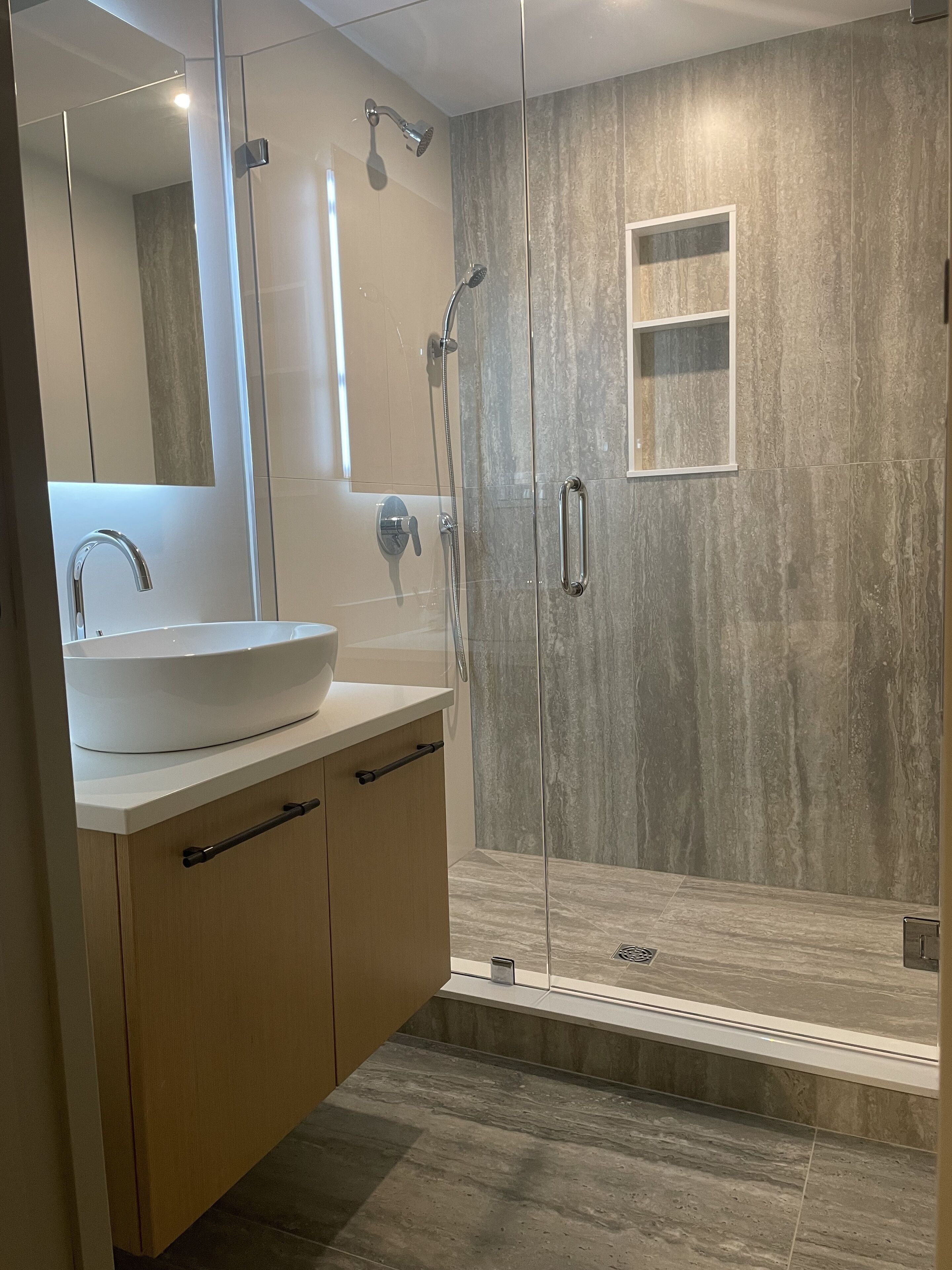 Un bany modern amb dutxa tancada amb vidre, un mirall gran i un lavabo blanc.