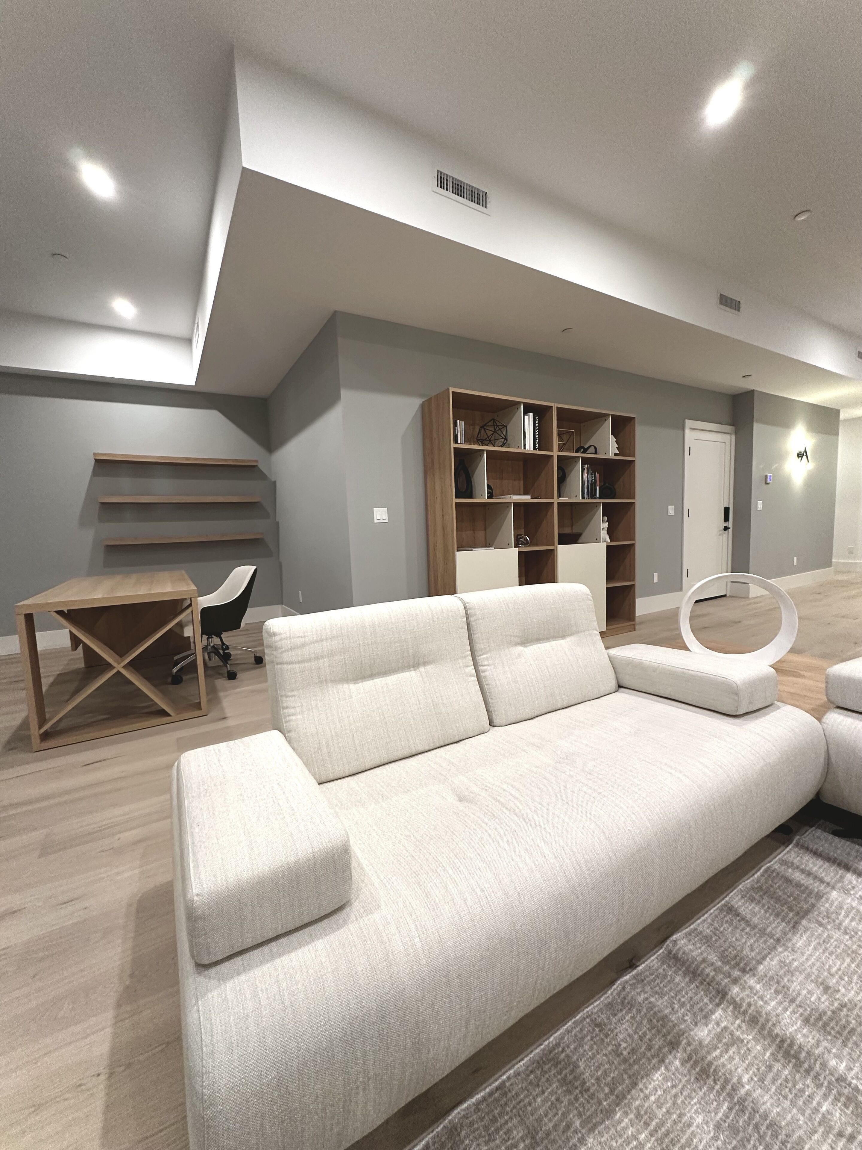 A modern living room with a sectional sofa, wooden shelves, and a desk.