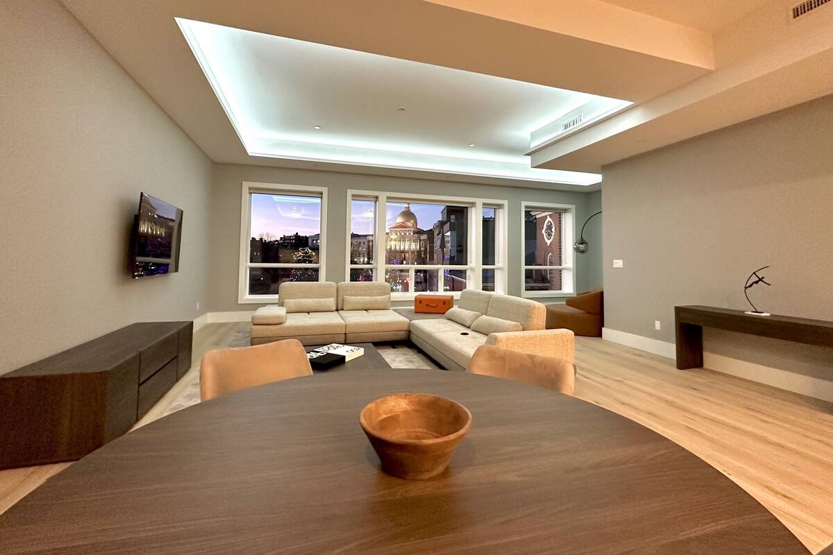 A modern living room with a large window, a sofa, a coffee table, and a dining table.