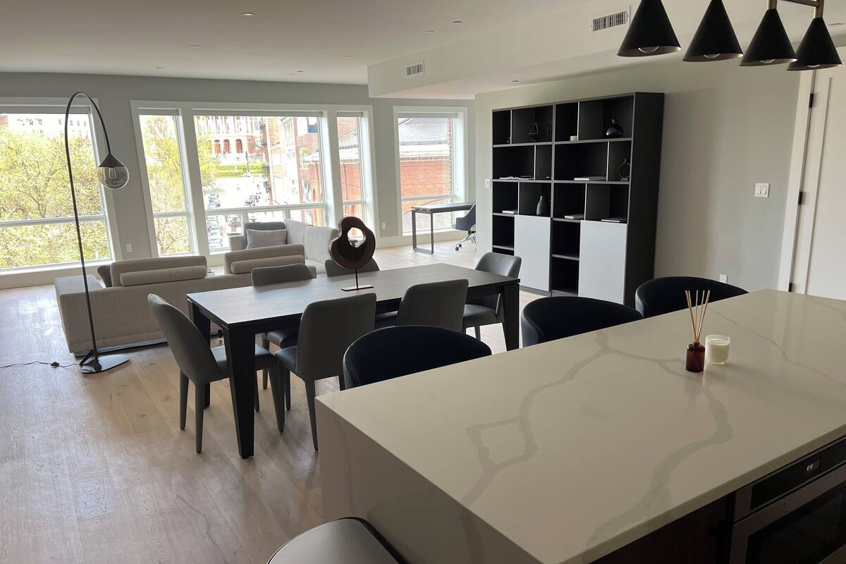 A modern kitchen with a central island, dining area with chairs, and a built-in bookshelf.