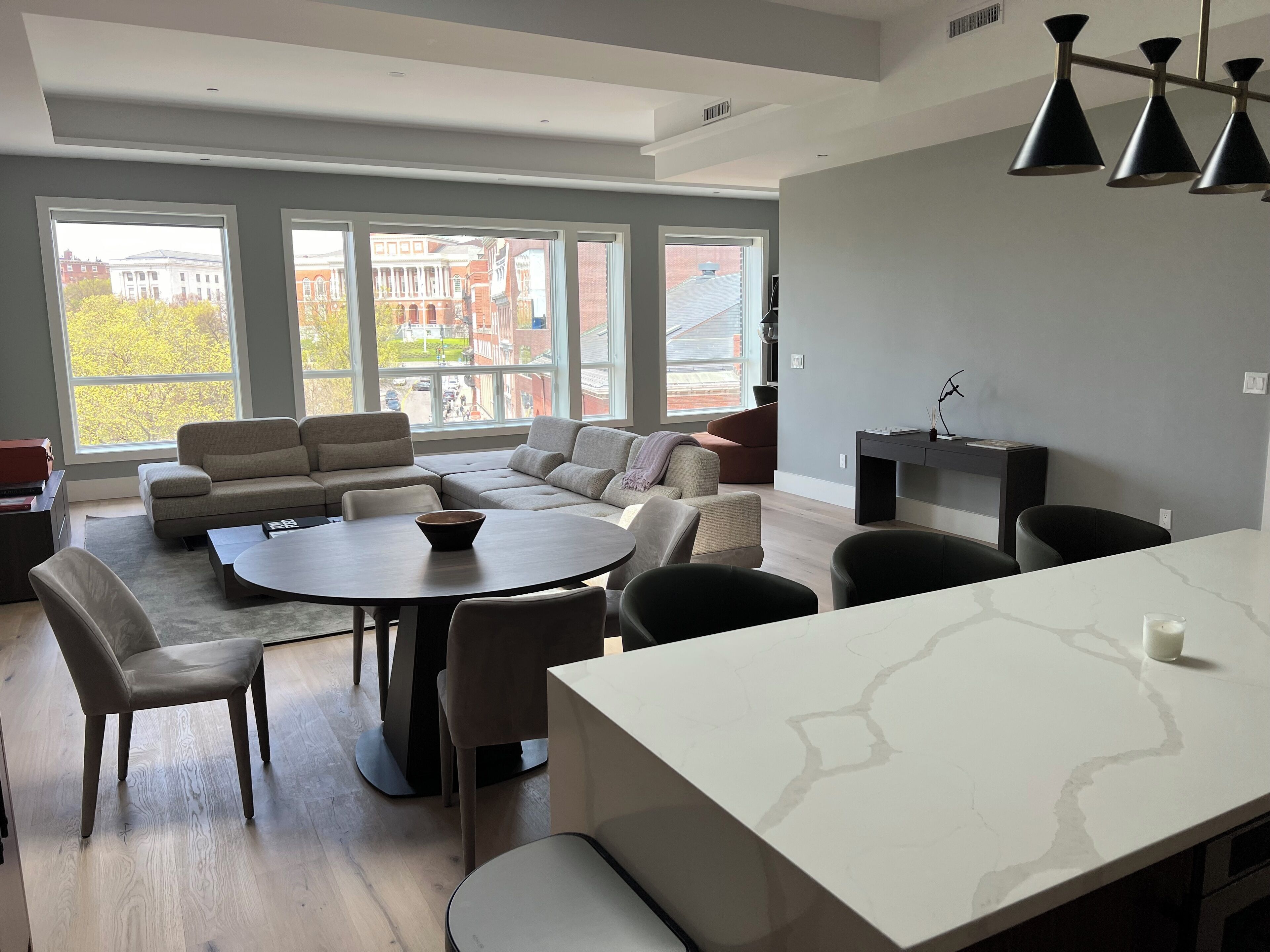 A modern living room with a sectional sofa, a round dining table, and a kitchen area with a white countertop.