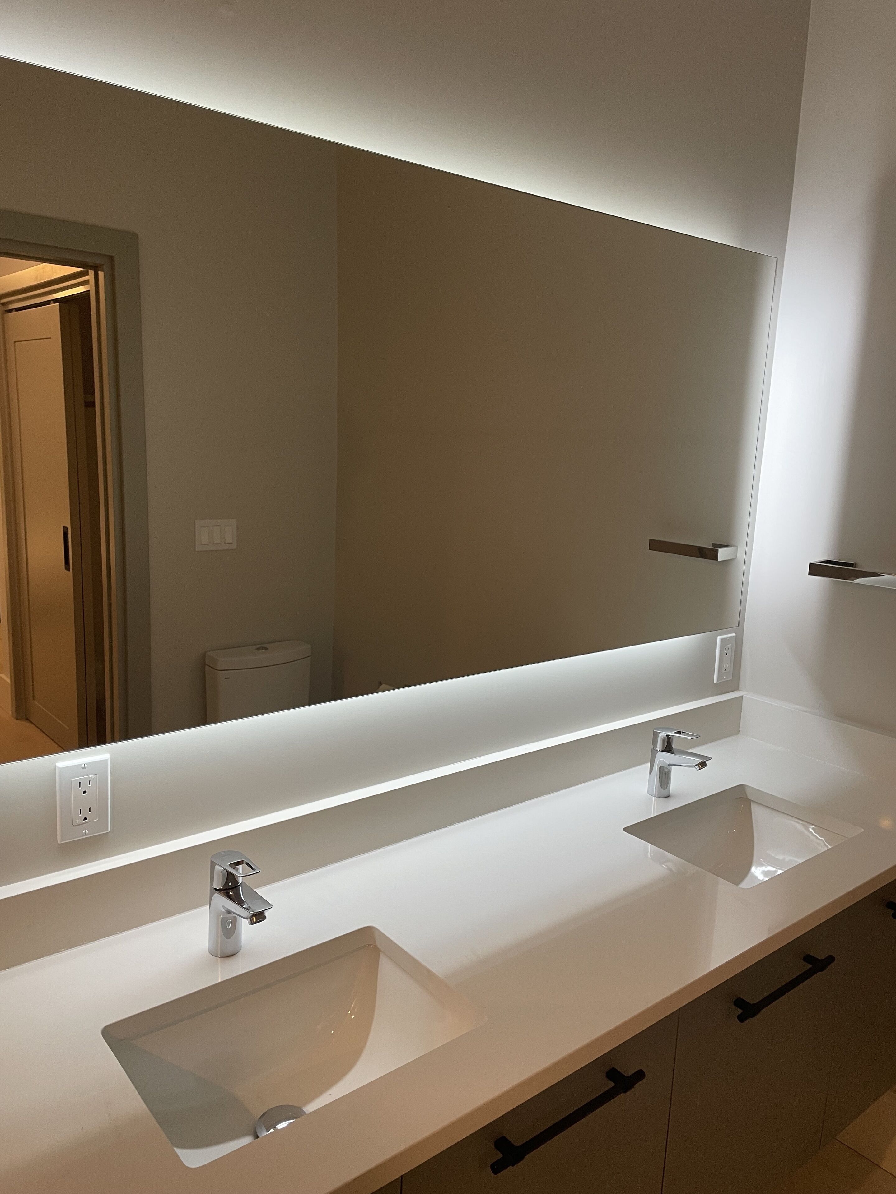 Un baño moderno con dos lavamanos, un espejo grande y un tocador iluminado.