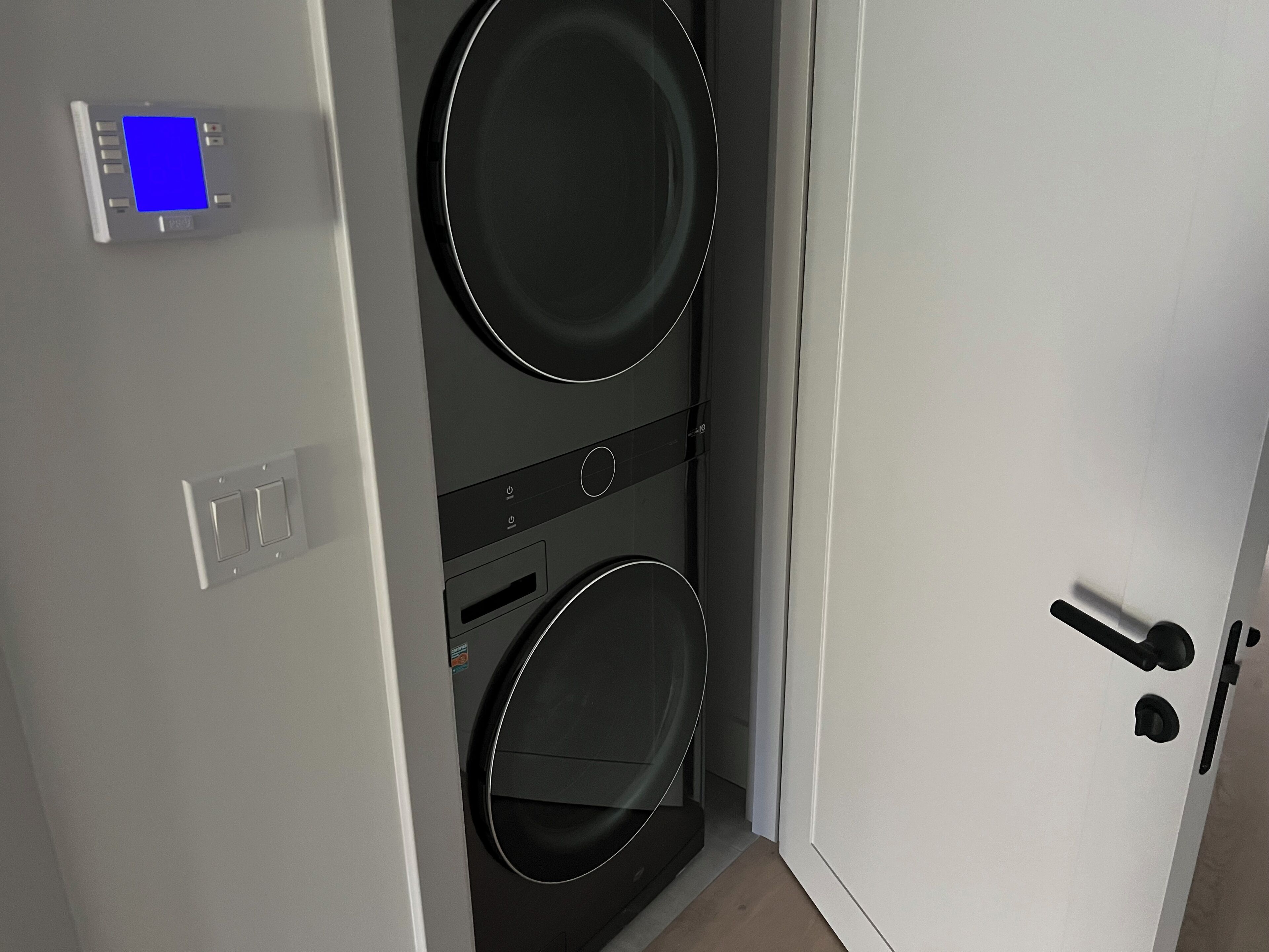A compact laundry room with two washing machines, a control panel, and a door.