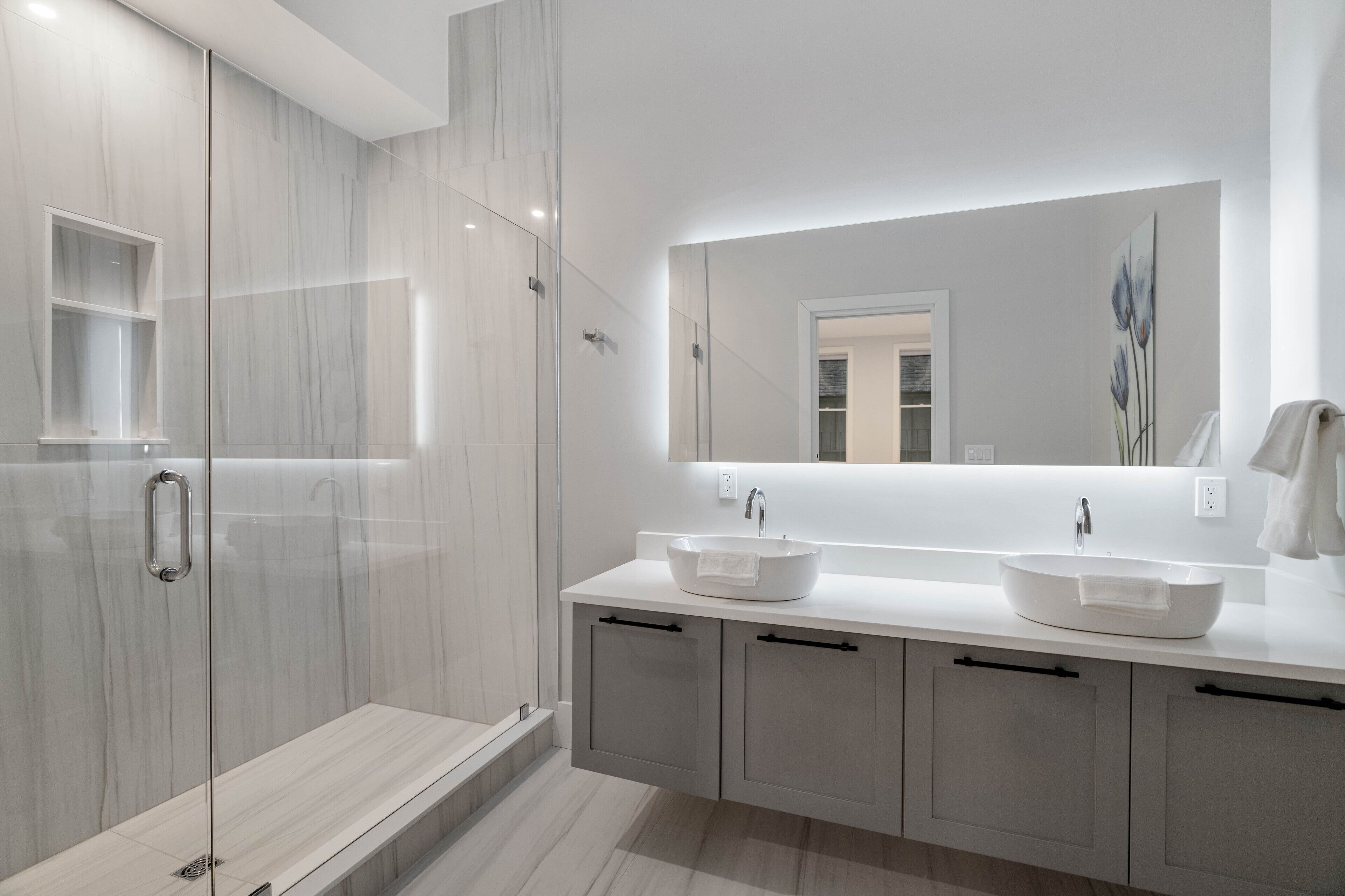 A modern bathroom with a glass-enclosed shower, two sinks, and a large mirror.