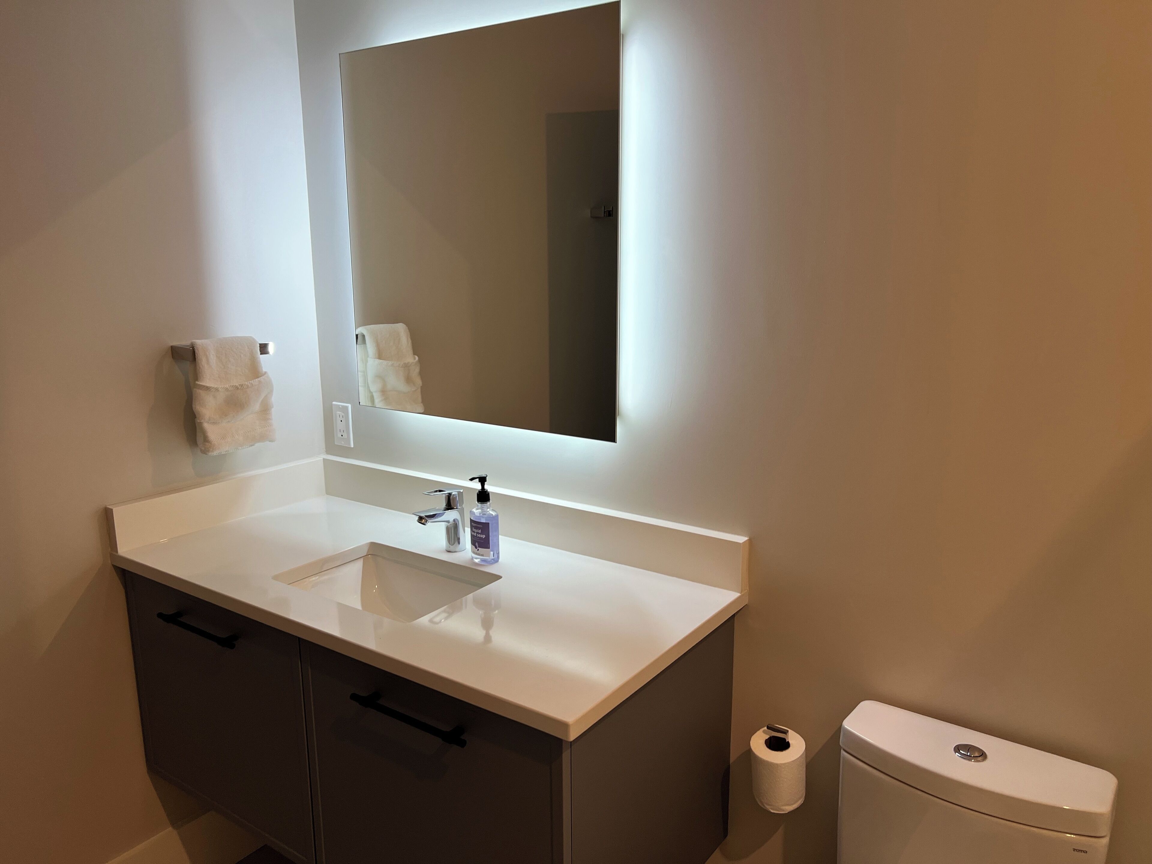 Une salle de bain avec un lavabo blanc, un miroir, une serviette et des toilettes.