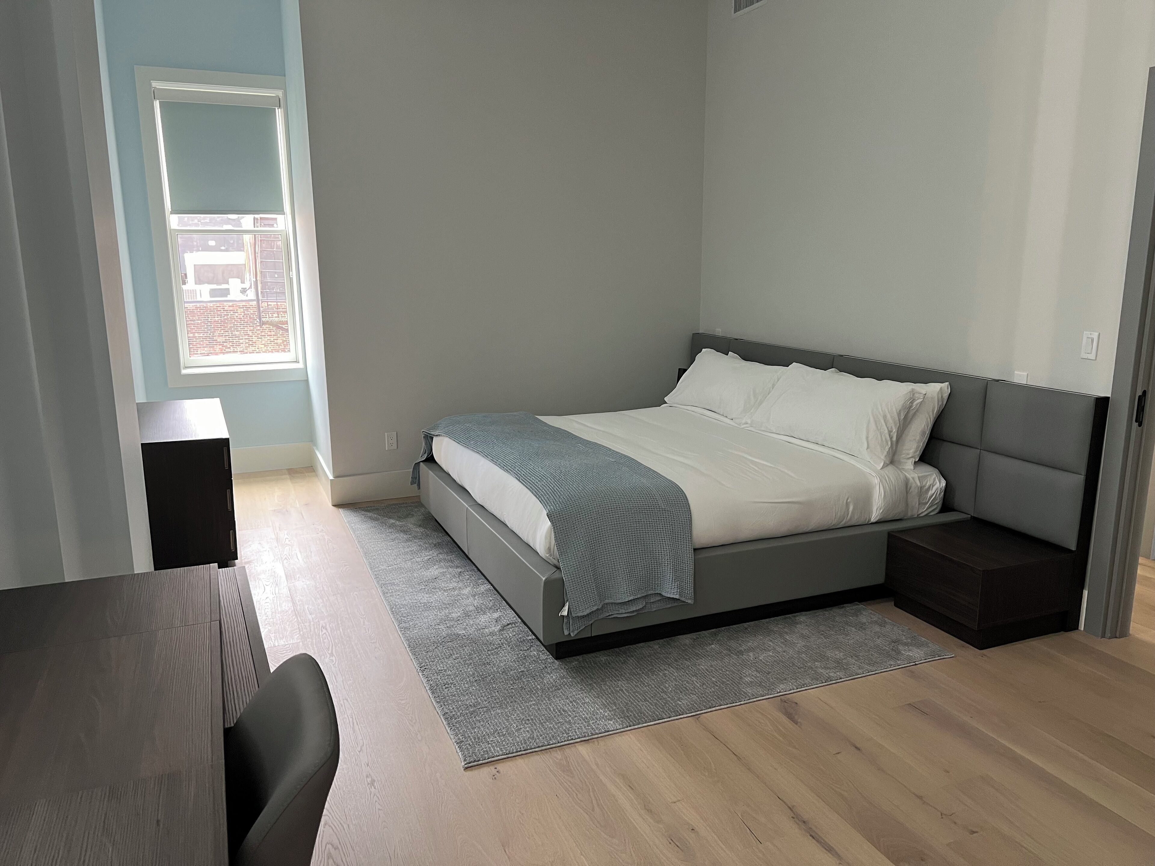 A modern bedroom with a bed, bedside tables, a desk, and a window.