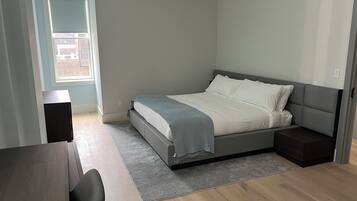 A modern bedroom with a bed, bedside tables, a desk, and a window.