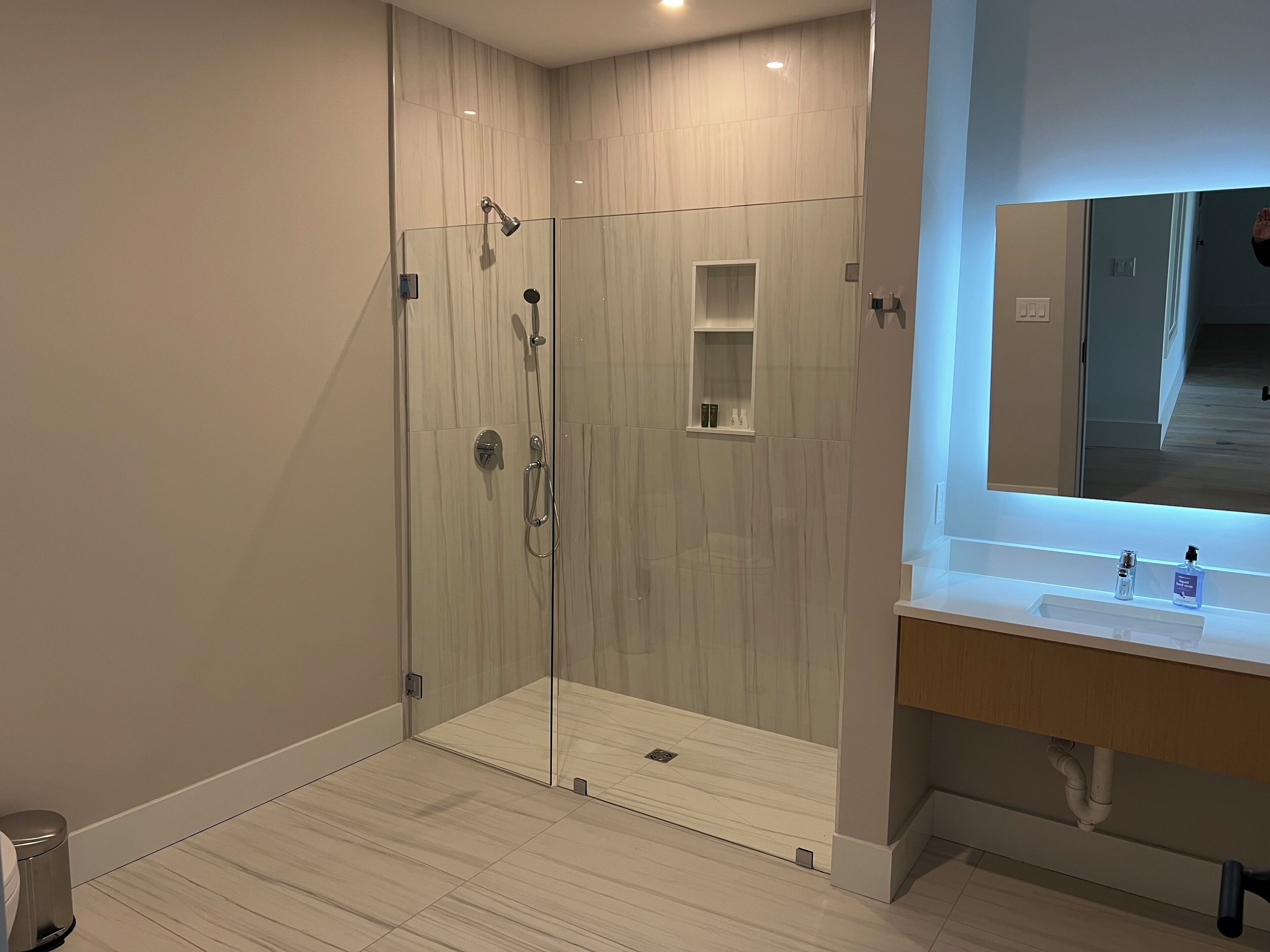 Ein modernes Badezimmer mit einer Duschkabine aus Glas, einem Waschtisch mit Spiegel und einer kleinen Ablage für Toilettenartikel.