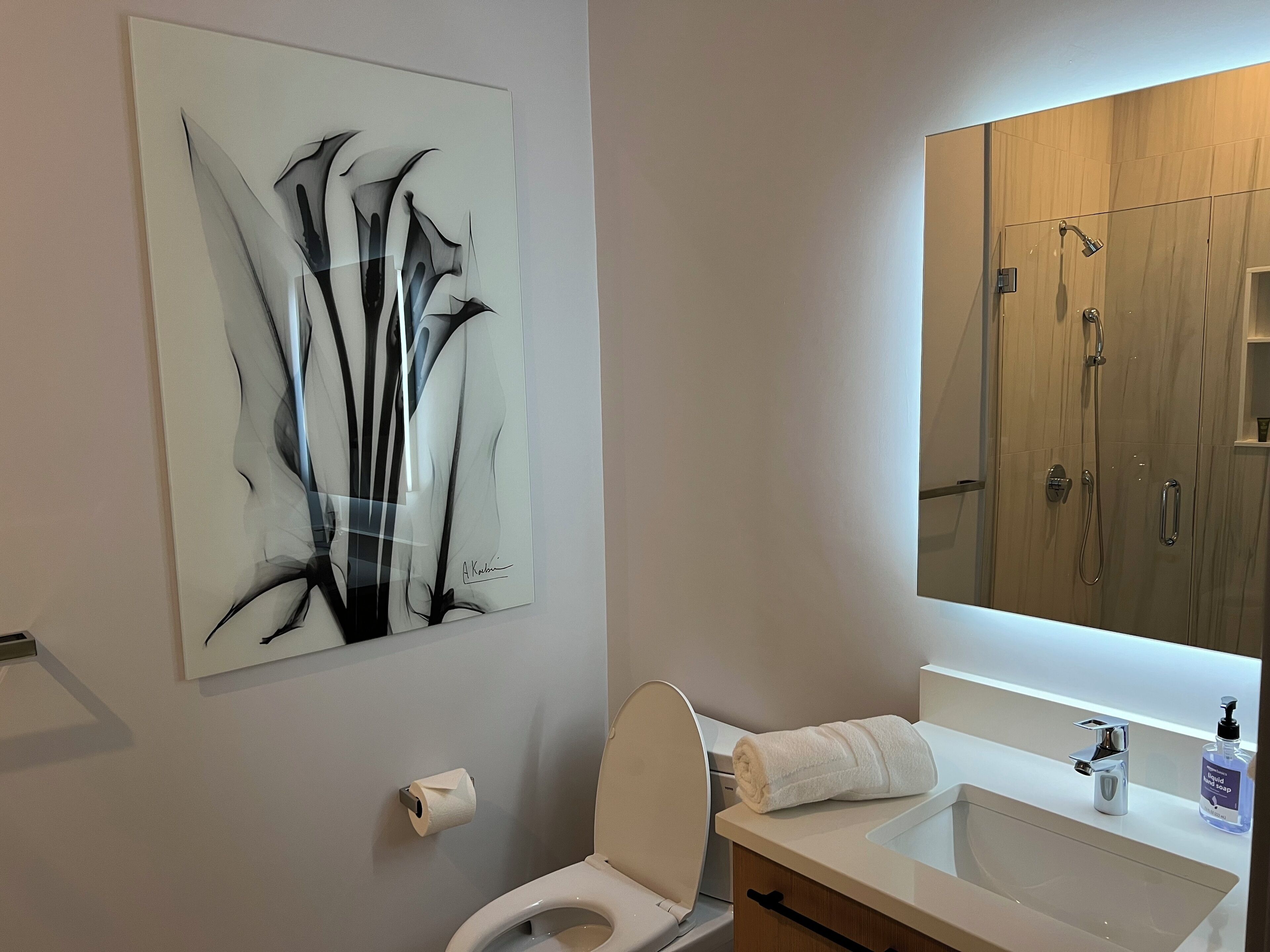 A modern bathroom with a toilet, sink, and shower. There's a large abstract painting on the wall and a mirror above the sink.
