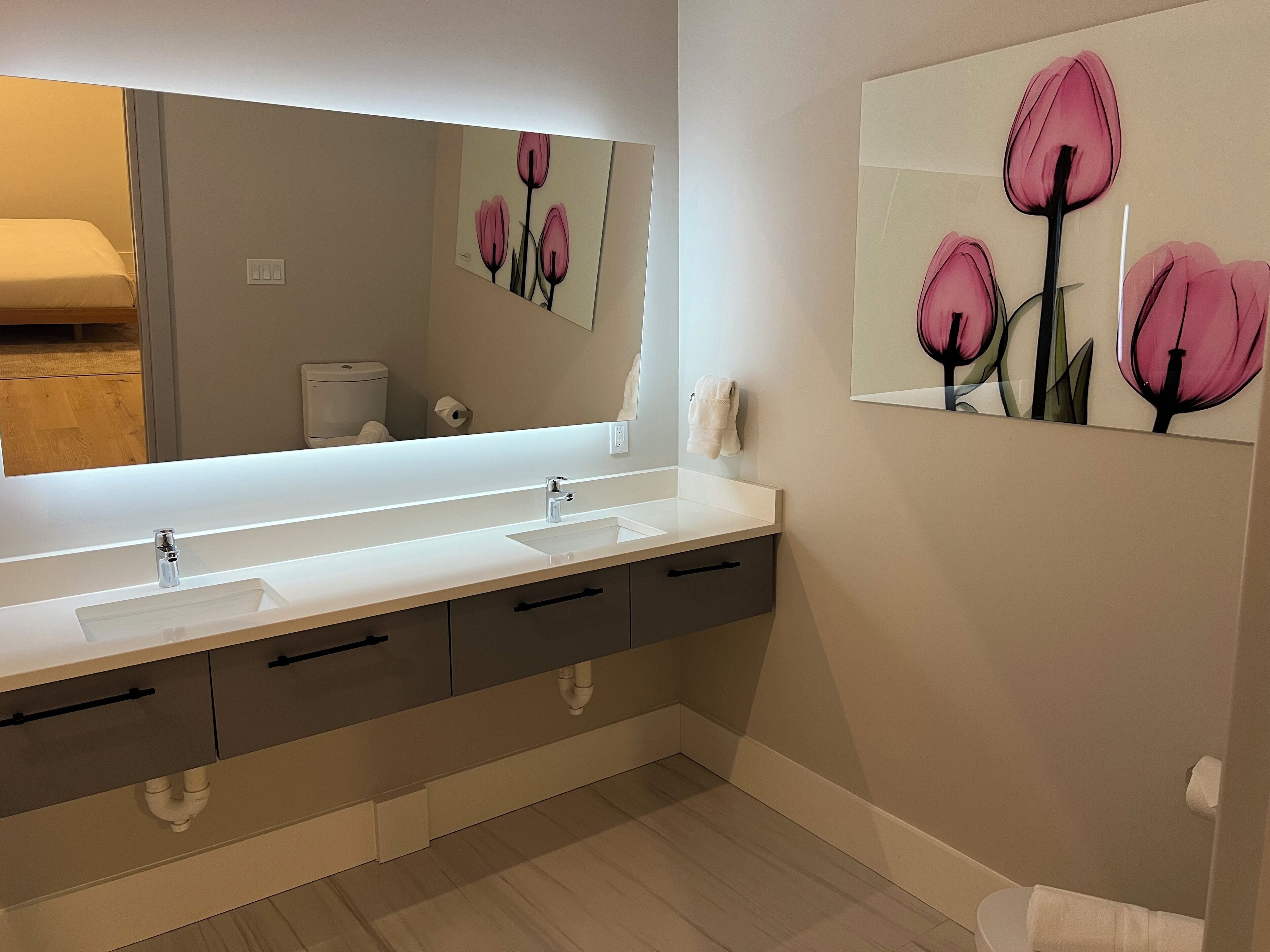 Un baño moderno con un lavamanos blanco, un espejo grande y un inodoro de pared.