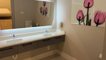 Un baño moderno con un lavamanos blanco, un espejo grande y un inodoro de pared.
