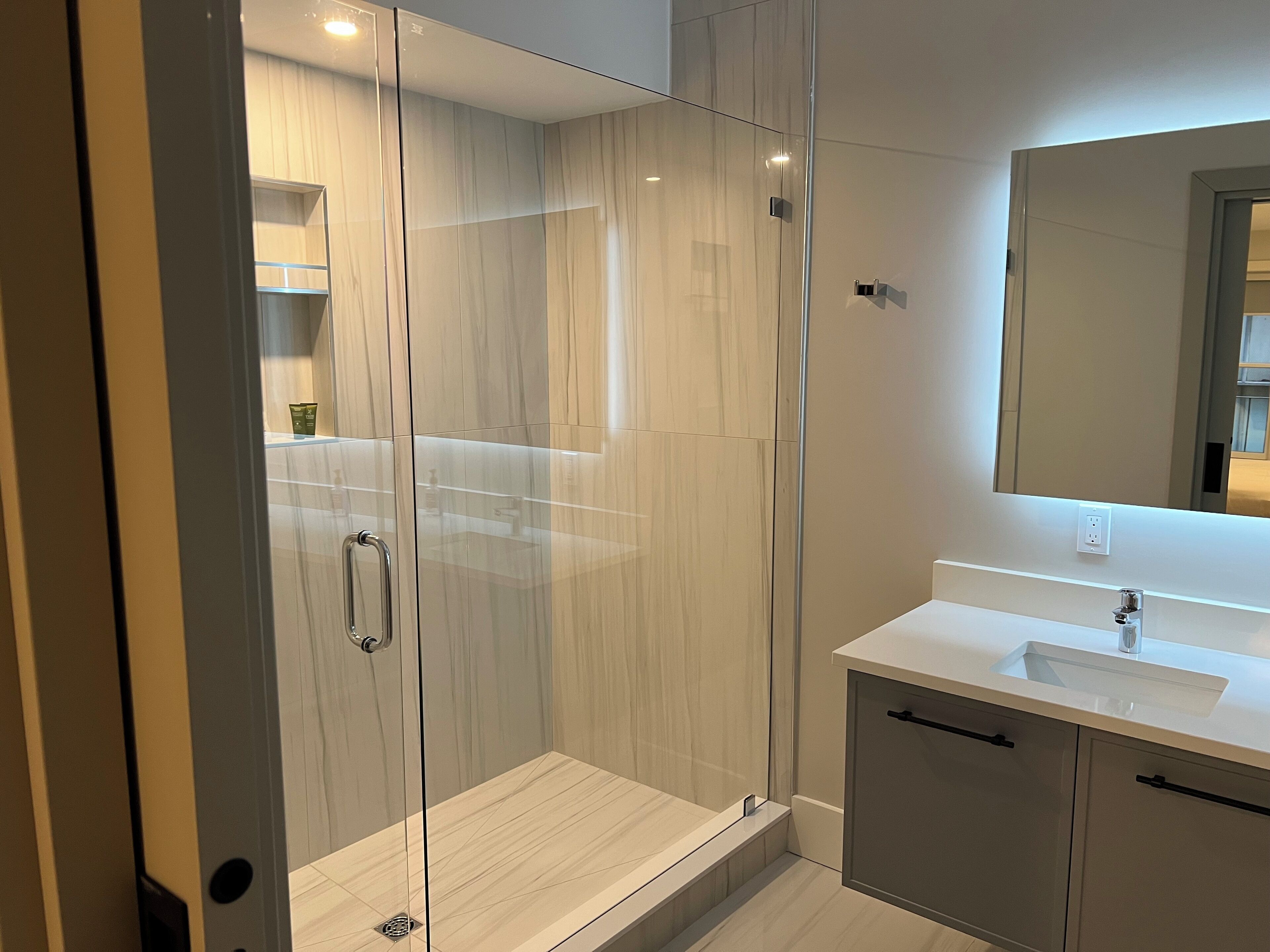 A modern bathroom with a glass-enclosed shower, a white sink, and a large mirror.