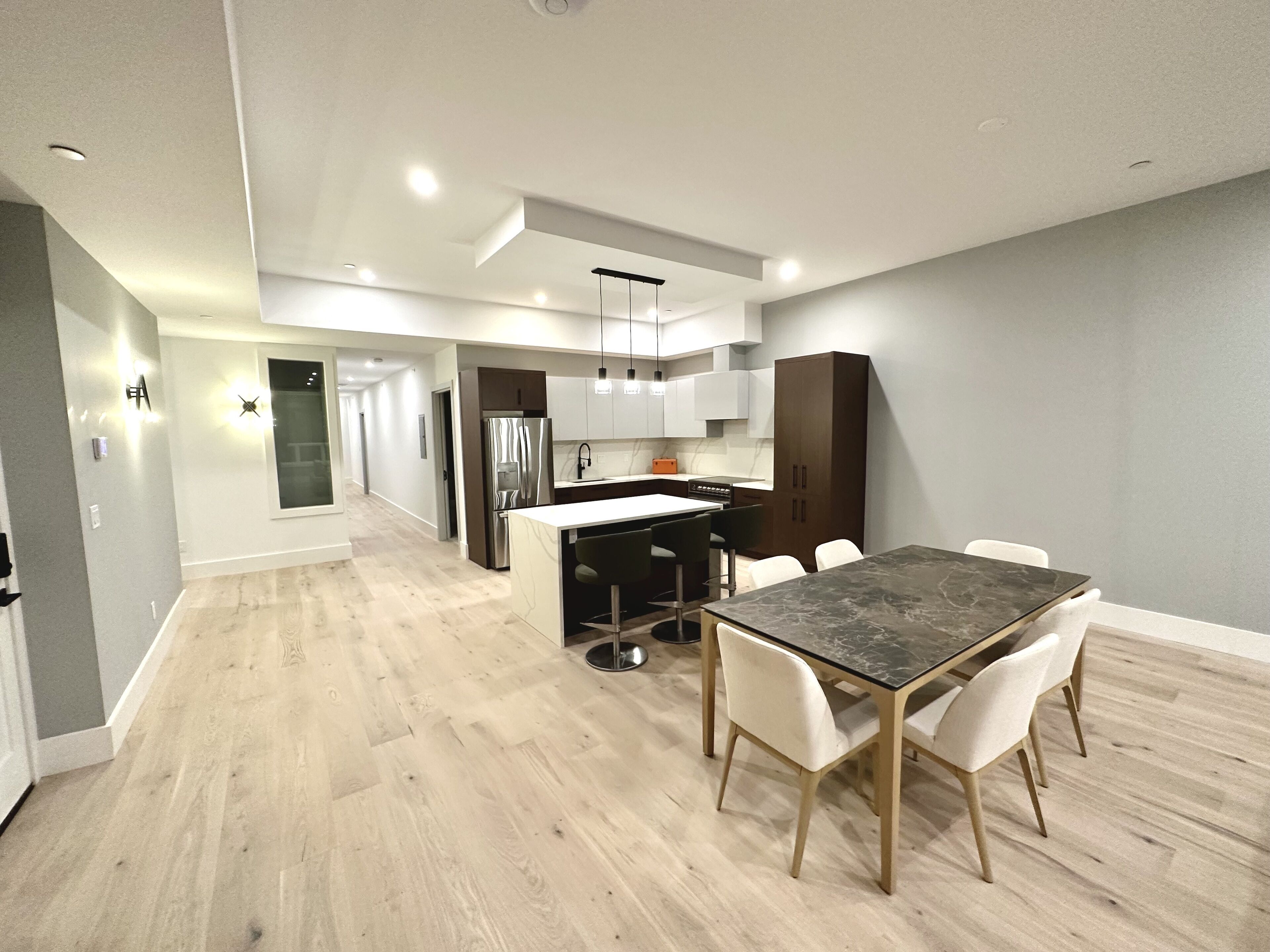 Una cocina moderna con una isla central, armarios blancos y un comedor con una mesa y sillas de mármol.