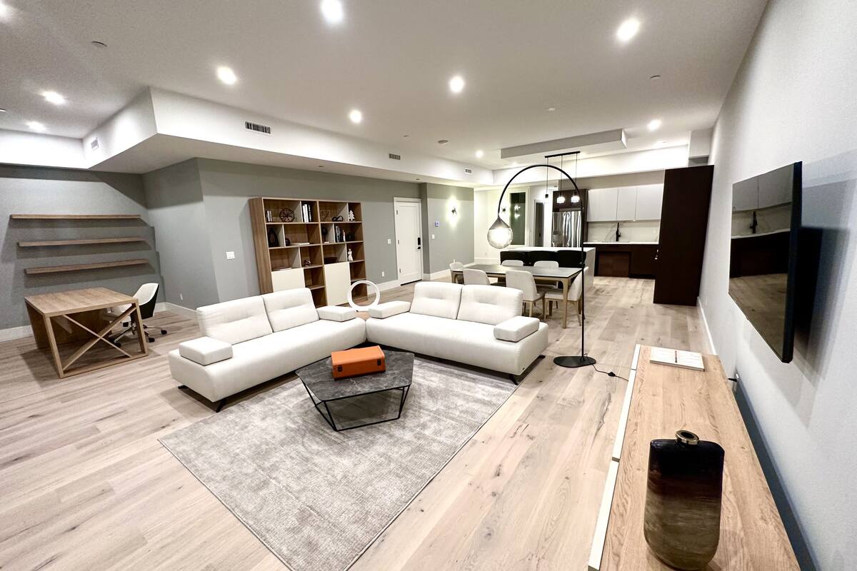 A modern living room with a sectional sofa, a coffee table, a dining area, and a kitchen.