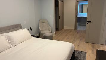 A bedroom with a bed, a chair, a small table, and a door leading to a bathroom.