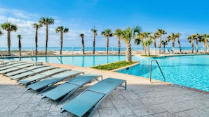 Un espace piscine avec des chaises longues et des palmiers, donnant sur une plage.