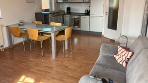 Et moderne køkken med hvide skabe, et spisebord med stole og en grå sofa med pude med striber.