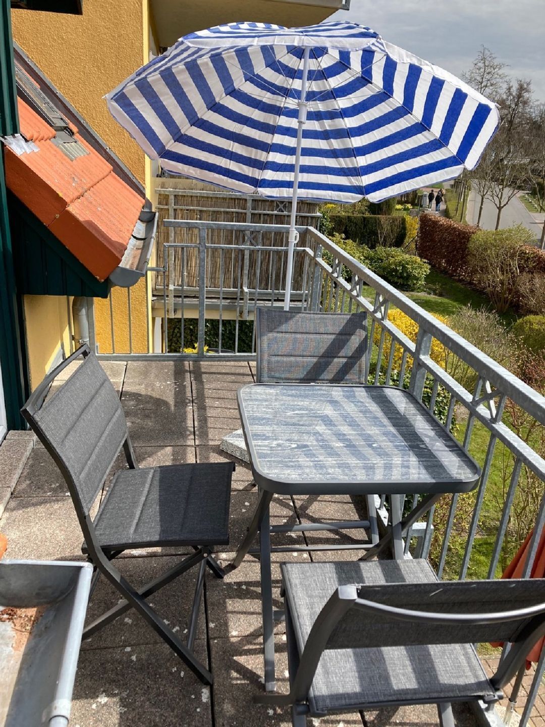 An outdoor patio with a blue and white striped umbrella, two metal chairs, and a small table.
