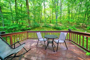 A wooden deck with a table and chairs, surrounded by a forest.