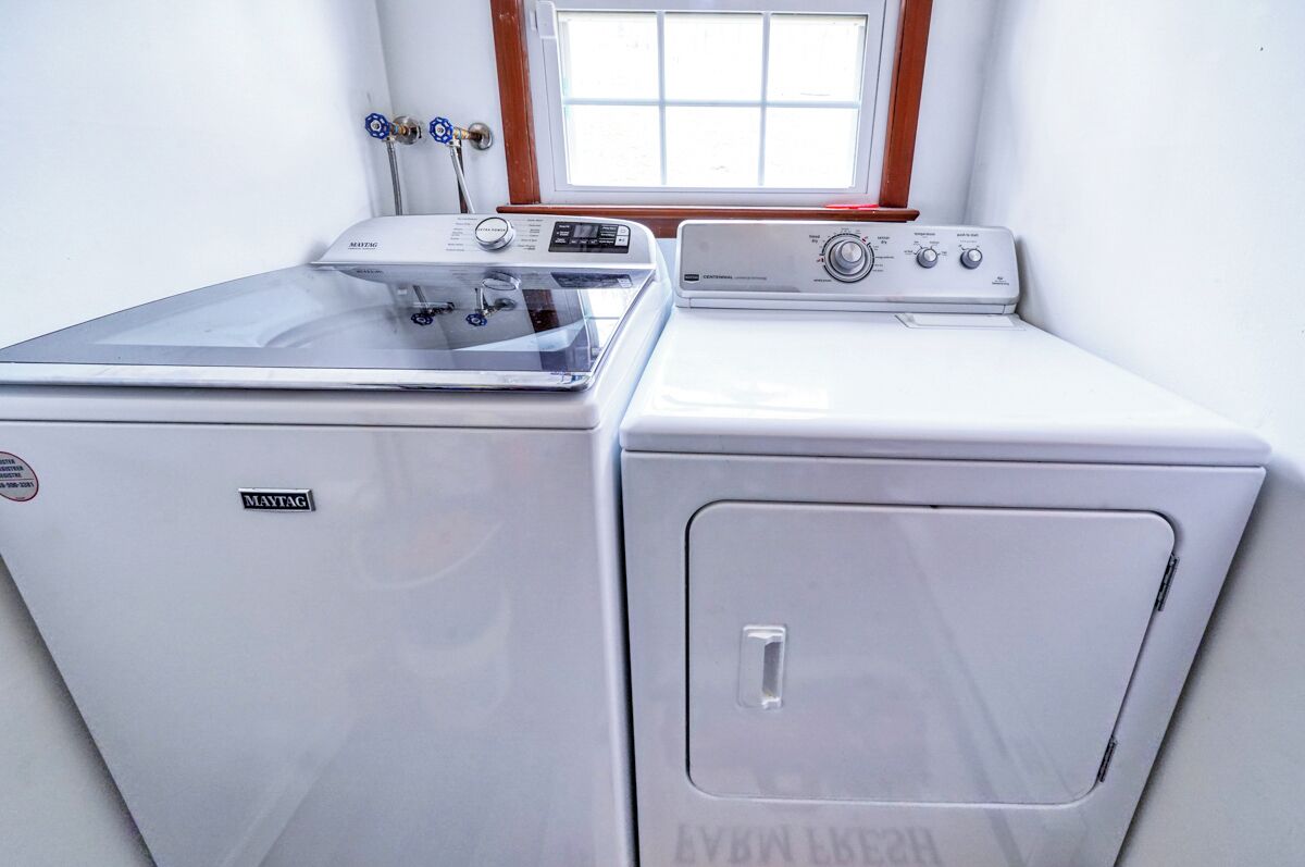 A compact laundry room with two Maytag washing machines and a dryer, a window above the machines, and a door with a handle.