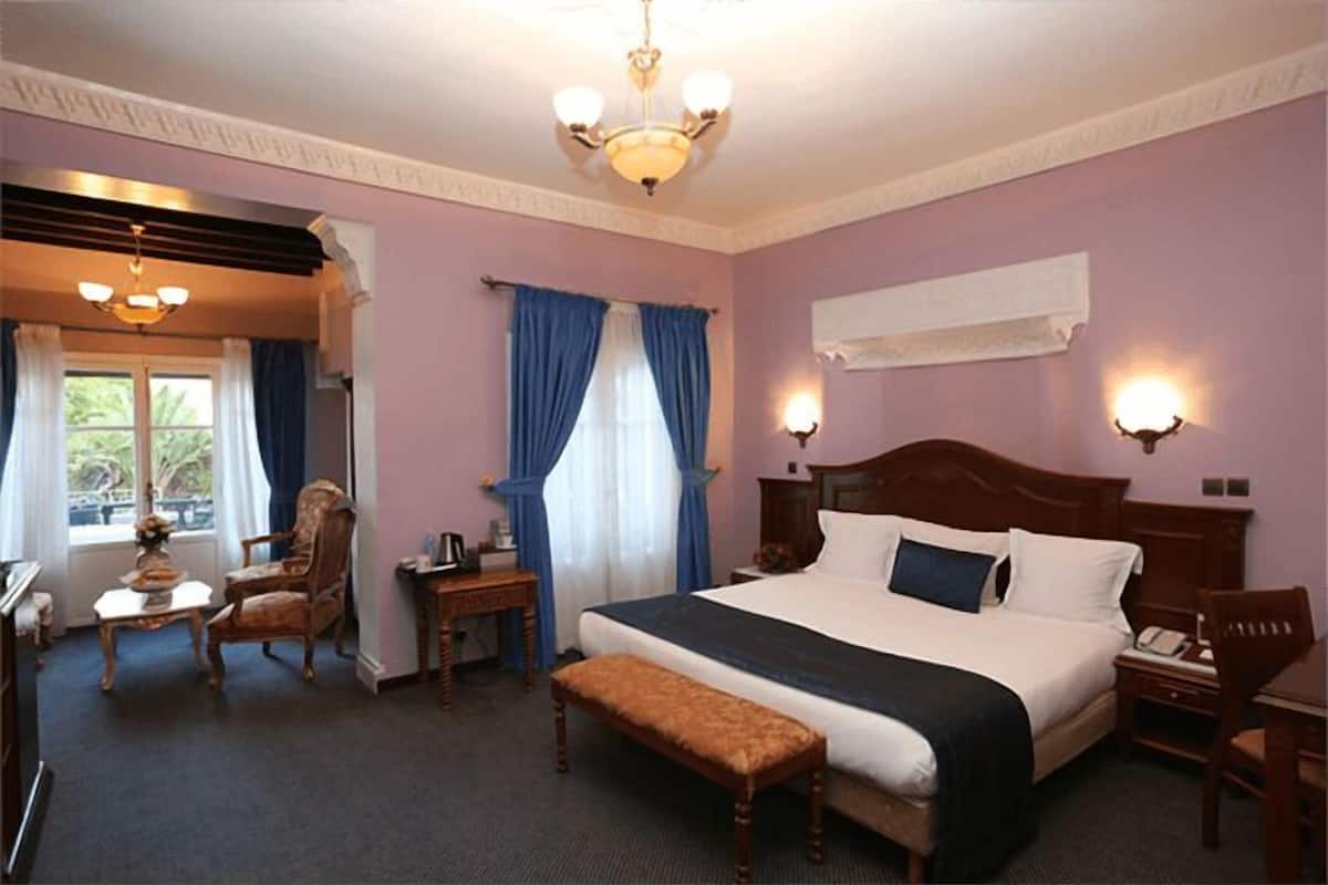 Habitació d'hotel amb un llit gran, un panell de fusta al capçal, una banca, un escriptori i una cadira.