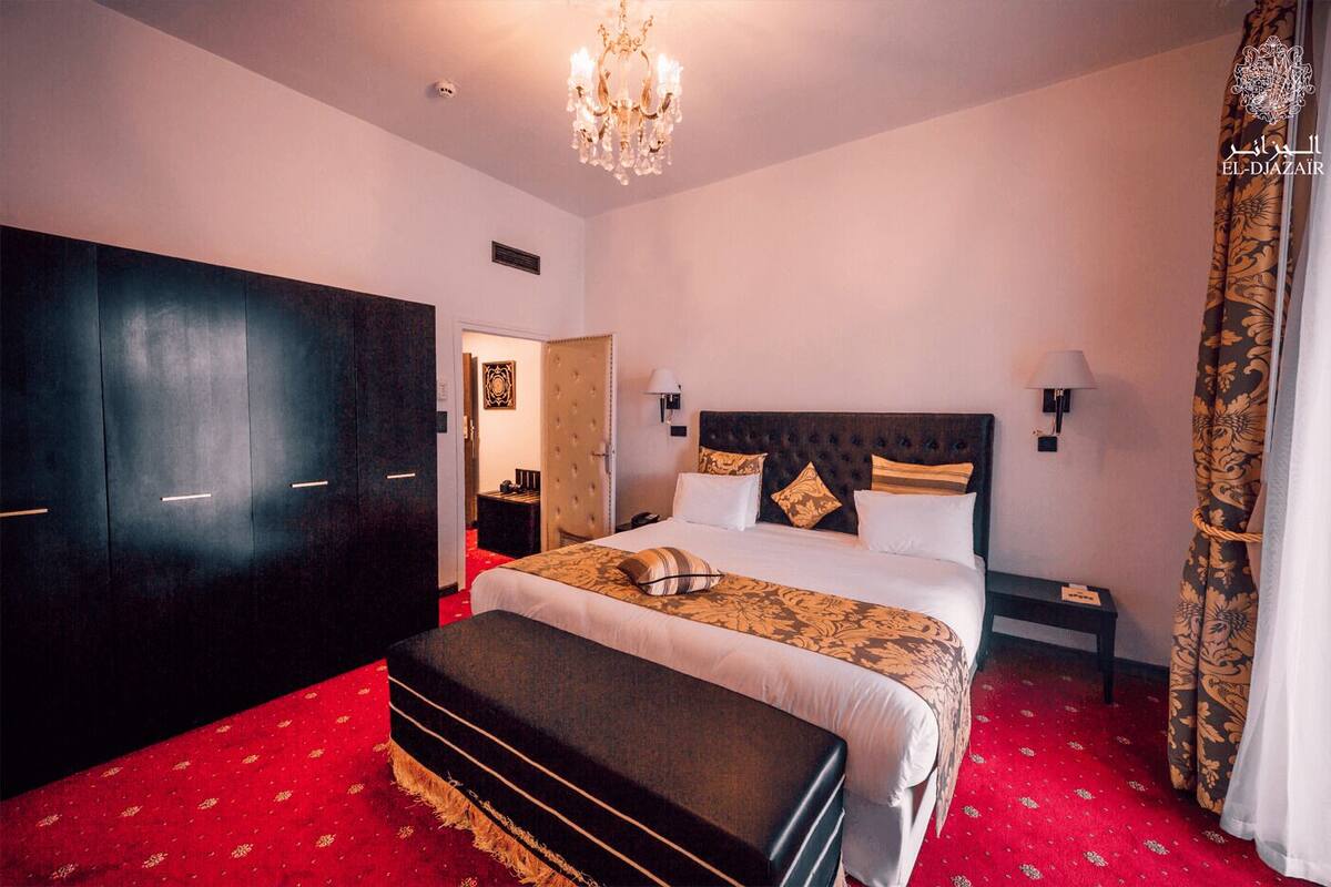 Habitació d'hotel amb un llit gran, un armari, una panxa, una tauleta de nit i un penjador de cristall.