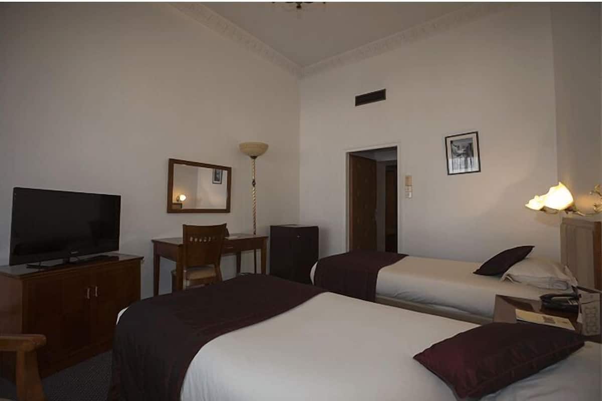 Una habitació d'hotel amb dos llits, un escriptori amb cadira, televisió, làmpada i un quadre al mur.