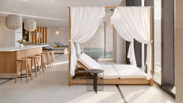 Un spa moderno con una cama de madera, un jacuzzi con paredes de cristal y una zona de bar con taburetes.
