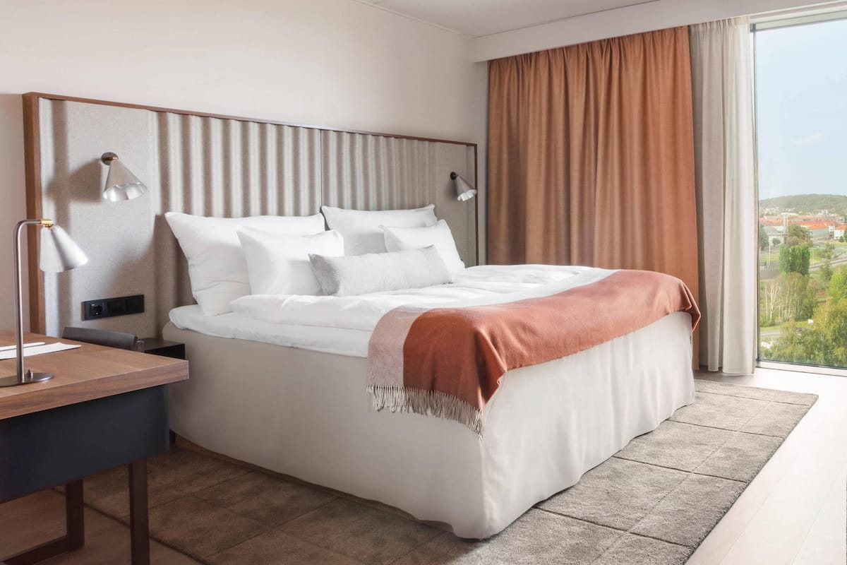 A modern hotel room with a large bed, a desk, and a view of the city.