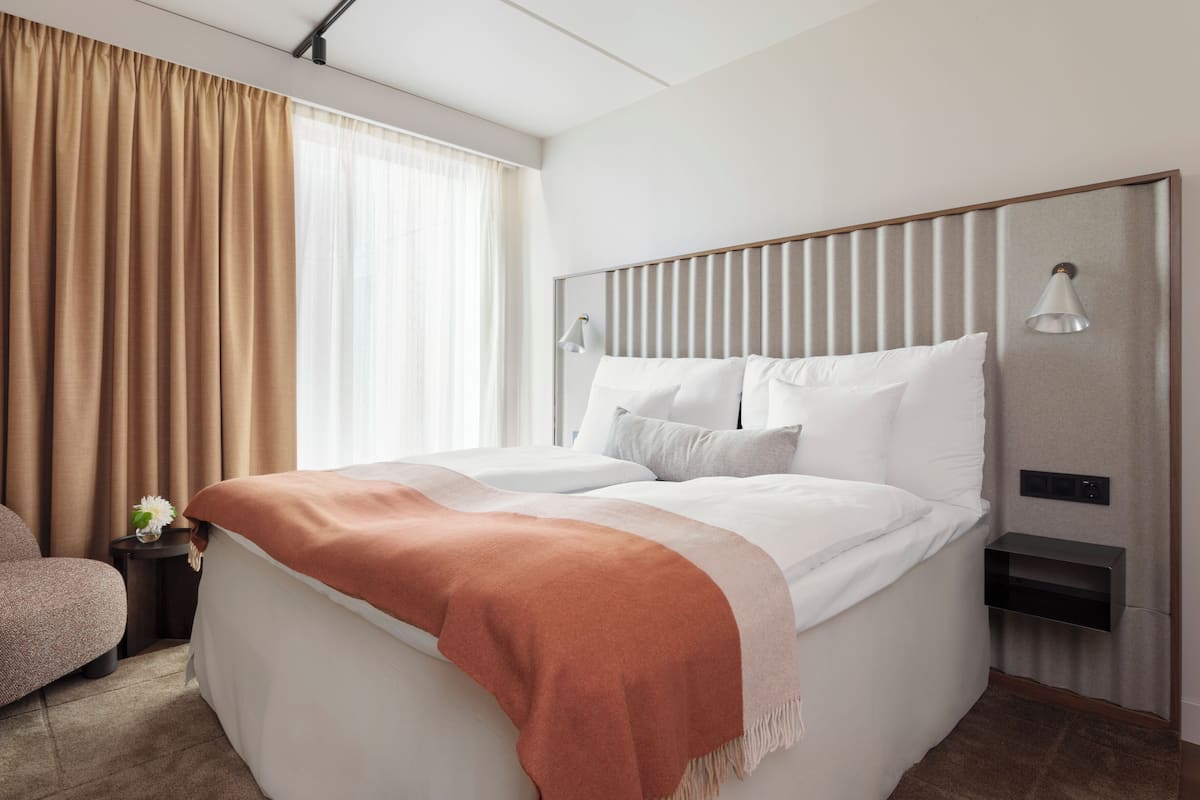 A neatly made bed with a headboard, a bedside lamp, and a small bedside table with a flower.