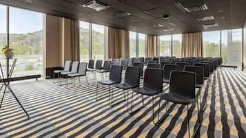 A conference room with rows of chairs, large windows, and a patterned carpet.