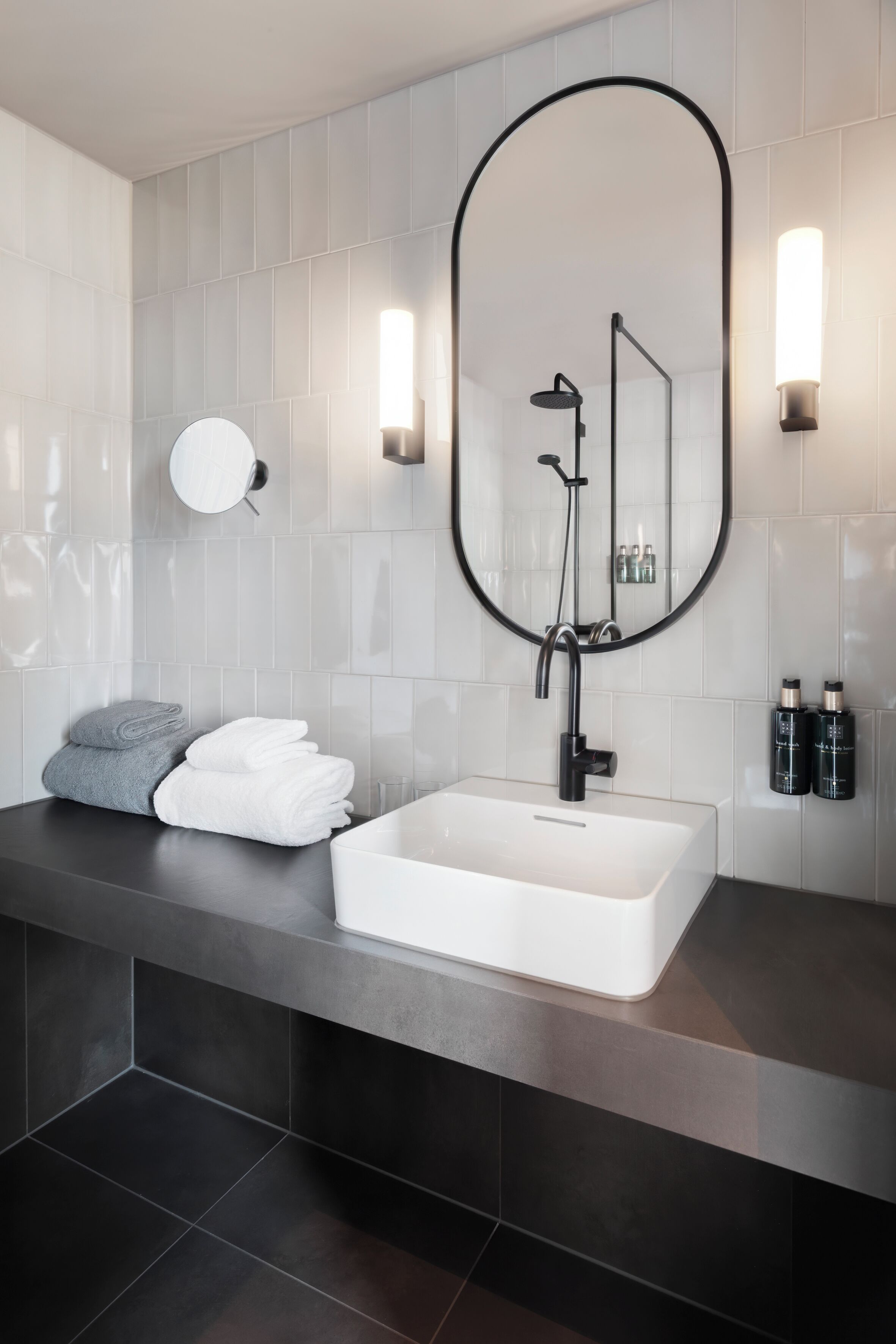 A modern bathroom with a white sink, dark countertop, and a large mirror.