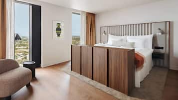 Habitación de hotel moderna con una cama grande, un armario de madera, zona de estar y vistas a la ciudad.